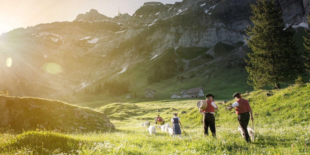 Appenzeller Bauern und Kinder laufen über eine saftige Schweizer Wiese mit Ziegen.