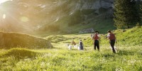 Appenzeller Bauern und Kinder laufen über eine saftige Schweizer Wiese mit Ziegen.